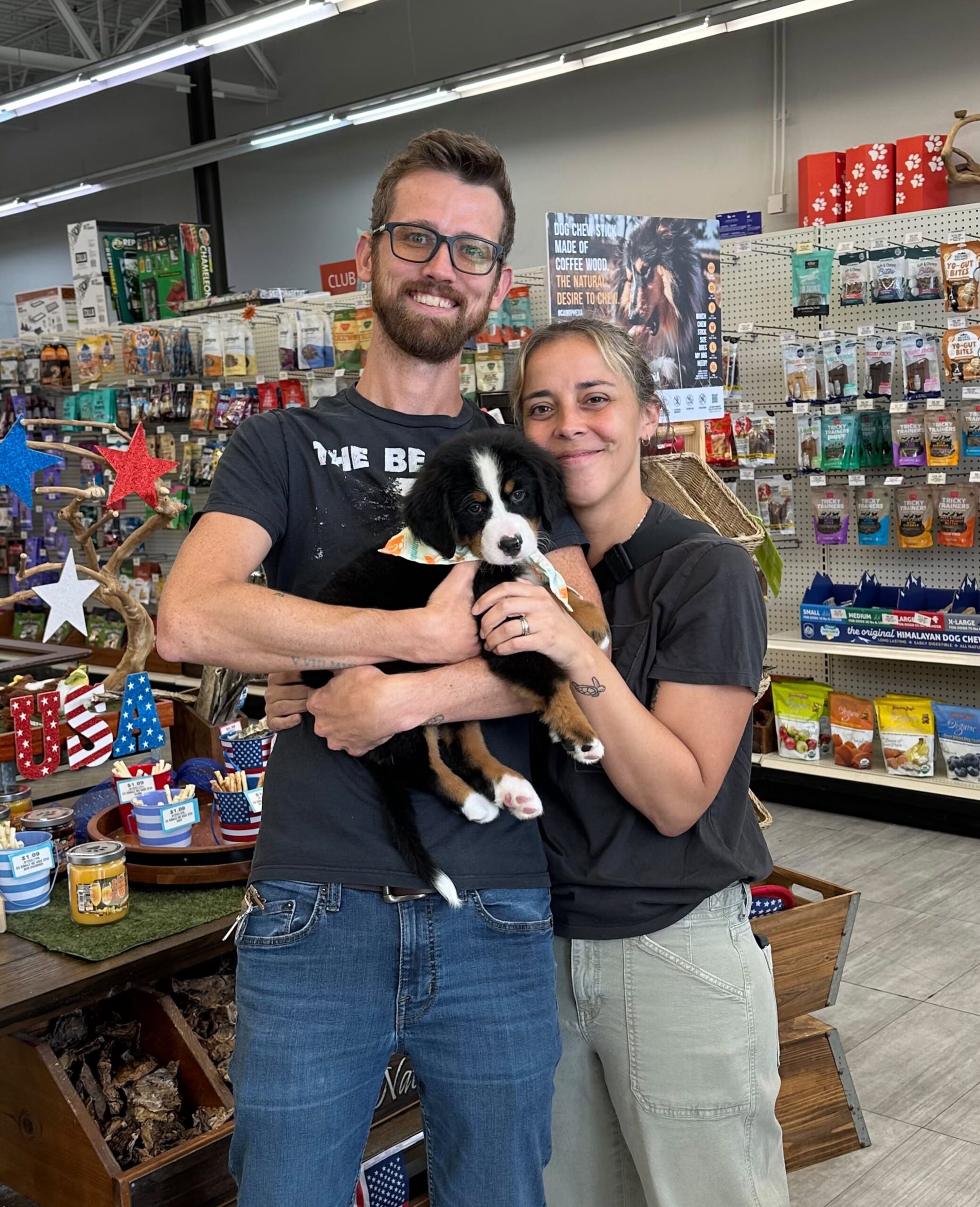 Two people holding a tricolor puppy inside a pet store